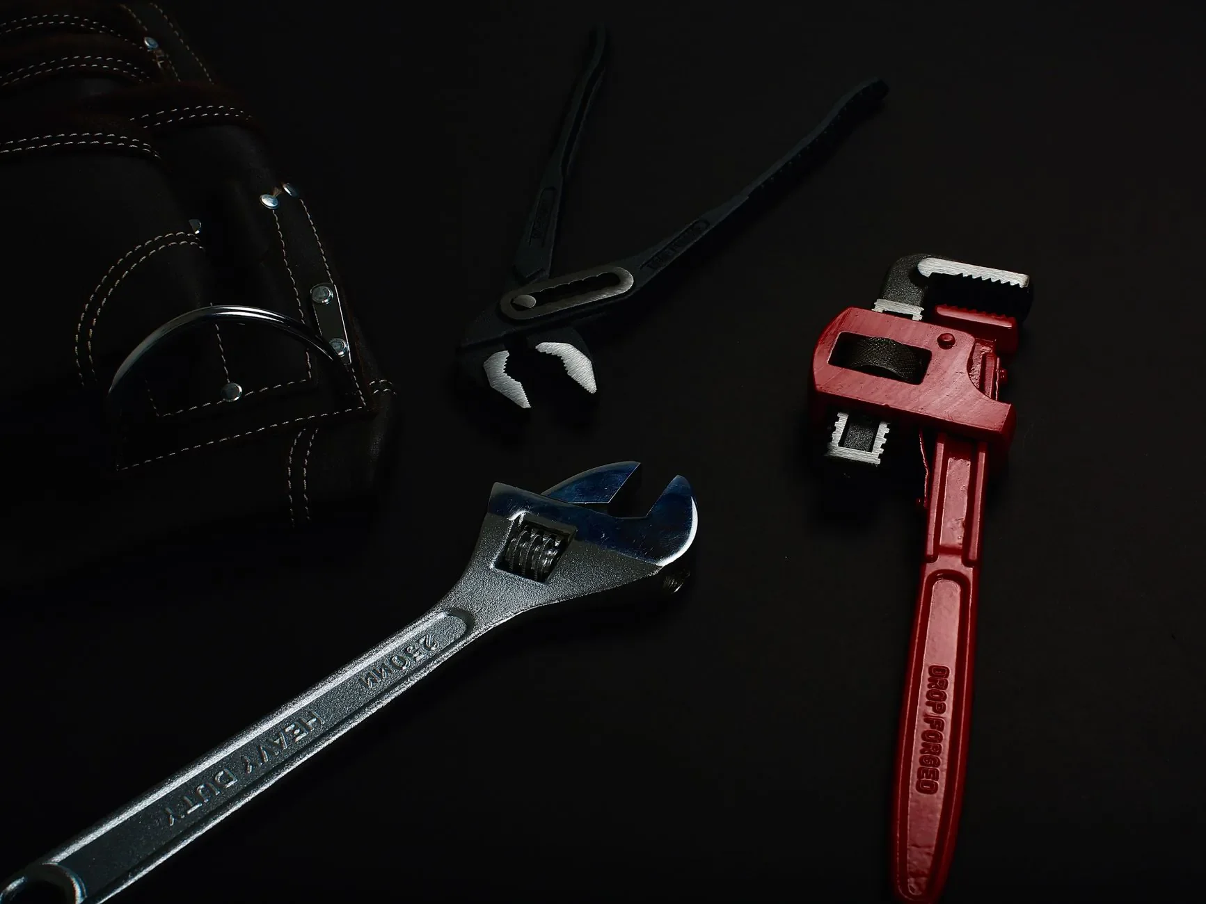 Gros plan de divers outils à main, y compris des clés et des pinces, sur une surface sombre.
