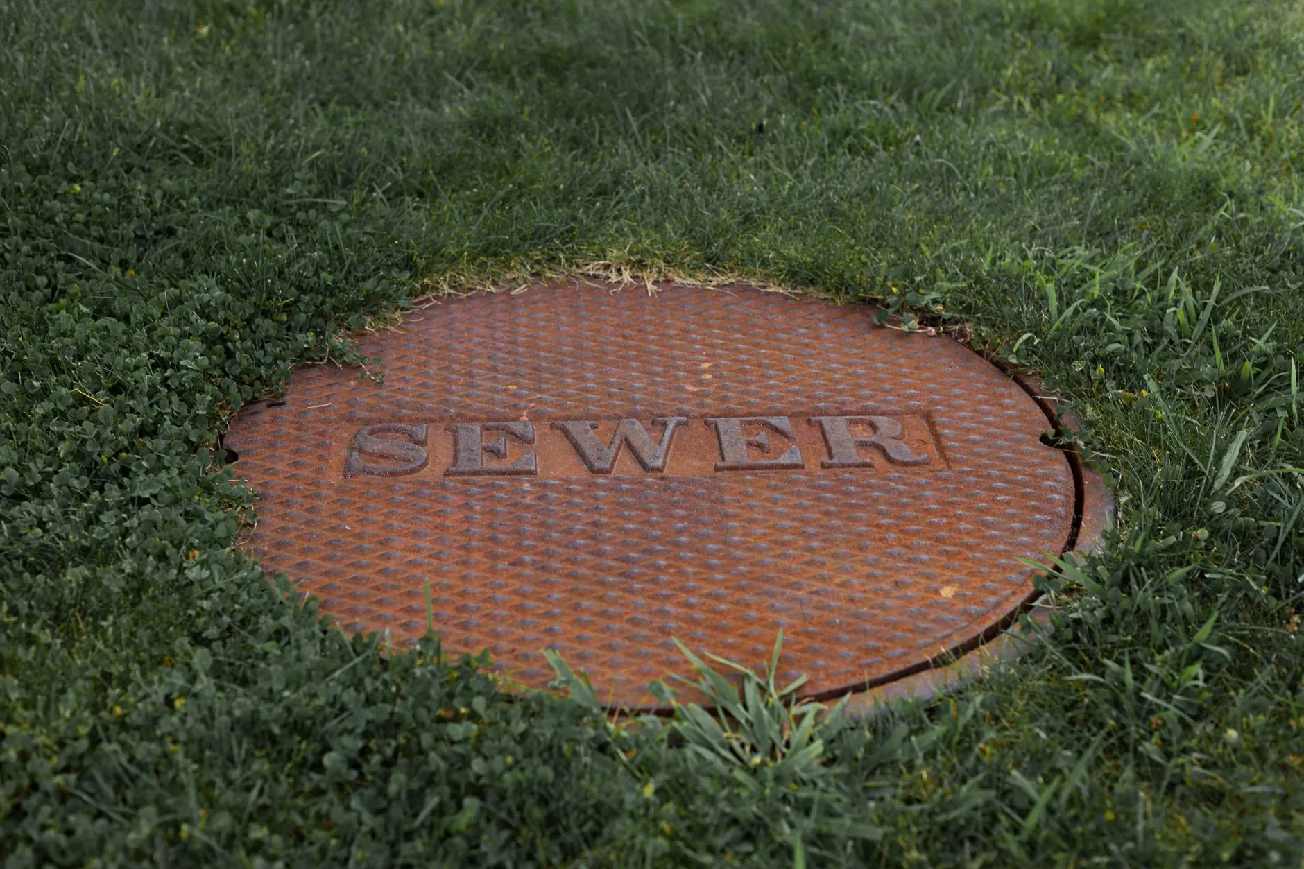 Gros plan sur un couvercle de regard des égouts rouillé dans un parc herbeux de Boston.