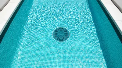 Vue plongeante sur une bonde de fond de piscine dans une eau cristalline avec reflets de soleil.